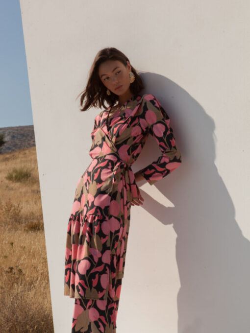 model wearing flory pink floral dress by mallory leaning on white wall